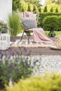 Cozy pillow with pattern and a pink blanket on a garden chair outside on a wooden terrace with rugs and plants