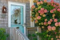 A cozy porch of a small wooden house and a lush blooming bush of pink hydrangea flowers nearby.