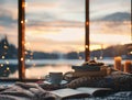 A cozy reading nook with soft blankets and a stack of books, with a beautiful sunset view over a calm lake with one cup of