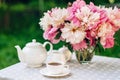 A cozy romantic breakfast in the open air. Peony flower vase, teapot and cup of tea on the table. Congratulations on mother`s day