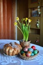 A cozy room - a table with a weave basket with Easter eggs, spring flowers and a sweet Easter bread Royalty Free Stock Photo