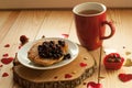 A cozy rustic composition with a red tea cup, a plate of pancakes with jam, and decorative hearts on a wooden surface