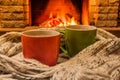 Cozy scene near fireplace with two cups of hot tea and cozy warm scarf. Royalty Free Stock Photo