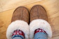 Cozy sherpa leather house slipperes with warm knit socks. Feet in slippers on wood floor. Room for copy space Royalty Free Stock Photo