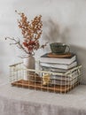 Cozy simple home interior - books in a metal basket, a ceramic cup, dried flowers in a vase on the table. Cozy home interior