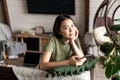 Cozy smiling asian girl sitting on sofa in living room, relaxing at home, using mobile phone and looking happy at camera Royalty Free Stock Photo