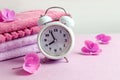 Cozy spring morning: white alarm clock with pastel hydrangea flowers on the background of a stack of terry towels