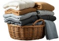A cozy stack of clean, folded sweaters in neutral colors next to a wicker basket isolated on white background Royalty Free Stock Photo