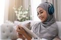 Cozy stay at home activities. young woman in hijab reading her favorite book, lying on sofa in living room. asian lady Royalty Free Stock Photo