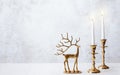 Cozy still life with burning candles and figure of deer on pastel light background. Christmas composition decoration of home