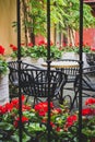 Cozy street cafe with iron fence in old town. Empty patio with outdoor furniture and red flowers. Royalty Free Stock Photo