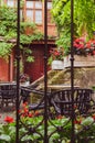 Cozy street cafe with iron fence in old town. Empty patio with outdoor furniture and red flowers. Royalty Free Stock Photo