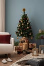 Cozy and stylish christmas living room interior with design armchair, christmas tree, gifts, wooden laterns, blue wall, red pillow Royalty Free Stock Photo