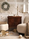 Cozy and stylish christmas living room interior with design armchair, retro shelf, poufm big window, christmas wreath, deer, gifts
