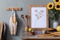 Cozy and stylish composition of creative dining room with mock up poter frame, wooden console, sunflower and personal accessories.