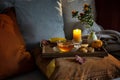 Cozy tea time in autumn served on a tray with candle, flowers and fall decoration on the couch with pillows in warm dark colors,