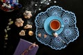 Cozy tea time: a cup of tea on a blue lace napkin, gingerbread, flowering willow branch, teapot, glasses on a book, black Royalty Free Stock Photo