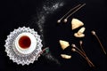 Cozy tea time: a cup of tea on a white lace napkin, homemade cakes, poppy seeds, black background, top view Royalty Free Stock Photo