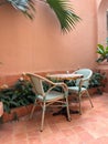 A cozy terrace features a small round table surrounded by two light-colored chairs. The backdrop is a warm peach wall Royalty Free Stock Photo