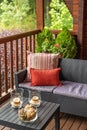 Cozy terrace with table and sofa at wooden cottage house surrounded by greenery and trees in countryside on cloudy Royalty Free Stock Photo