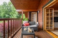 Cozy terrace with table and sofa at wooden cottage house surrounded by greenery and trees in countryside on cloudy Royalty Free Stock Photo