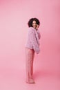 Cozy vertical shot in studio in pink colour. Girl with bare feet in striped wide trousers and fur c