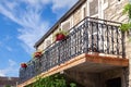 Cozy vintage French balcony with black metal railings, flowers in pot, open shutters on windows against blue sky, clouds. Bottom Royalty Free Stock Photo