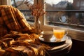 Cozy warm autumn composition with cup of hot tea, cozy plaid blanket and autumn leaves by a window on sunny day. Autumn home decor Royalty Free Stock Photo