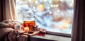 Cozy warm Christmas arrangement with a cup of hot tea, a cozy blanket and Christmas decorations by the window on a sunny winter