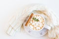 Cozy warm knitted scarf and cacao with marshmallows and cinnamon in vintage cup. White table, top view, flat lay