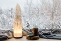 Cozy winter home set with natural selenite crystal electric tower lamp illuminated on window sill.