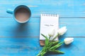 Cozy winter relax time.  Cup of hot coffee with write note on paper and lily flower on the blue wood background in morning sunny d Royalty Free Stock Photo