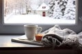 Cozy winter still life cup of hot coffee and opened book with warm plaid on vintage windowsill of cottage against snow landscape Royalty Free Stock Photo