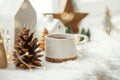 Cozy winter still life. Stylish cup of tea with modern christmas decoration, pine cone, wooden star and tree, golden lights on Royalty Free Stock Photo