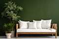 Cozy wooden sofa with white cushions near dark green wall. Side table with houseplant and potted tree Royalty Free Stock Photo