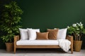 Cozy wooden sofa with white cushions near dark green wall. Side table with houseplant and potted tree Royalty Free Stock Photo