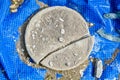 Cracked cement disc on blue reinforced checkered PVC material in debris