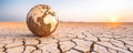 A cracked earth landscape with a globe symbolizing climate change and environmental challenges under a beautiful sunset Royalty Free Stock Photo