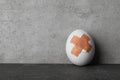 Cracked egg with sticking plasters on grey stone table, space for text Royalty Free Stock Photo