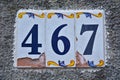 A cracked house number plaque, showing the number four hundred sixty seven 467