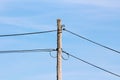 Cracked old wooden utility pole with thin black electrical wires connected with metal holders insulated with rubber