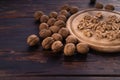 Cracked and whole walnuts on round wooden plate and wooden table, side view. Healthy nuts and seeds composition. Royalty Free Stock Photo