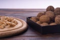 Cracked and whole walnuts on round wooden plate and wooden table, side view. Healthy nuts and seeds composition. Royalty Free Stock Photo