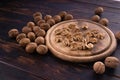 Cracked and whole walnuts on round wooden plate and wooden table, side view. Healthy nuts and seeds composition. Royalty Free Stock Photo