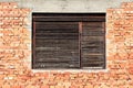 Cracked wooden window blinds on old dilapidated window frame mounted on red brick and concrete wall of abandoned family house Royalty Free Stock Photo