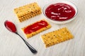 Crackers with flax seeds, white bowl with cherry jam, cookie with jam, spoon with jam on table