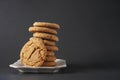 A crackly gingerbread cookie leans against a stack of cookies on a white plate with black background Royalty Free Stock Photo