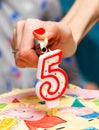 Female hand lighting a number 5 candle on a birthday cake using a lighter macro, closeup. 5th bday, five years old kids party