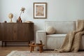 Craeative composition of living room interior with mock up poster frame, beige sofa, wooden commoda, brown plaited plaid, vase