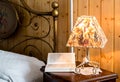 Craft bedside lamp and a book on a bedside table in bedroom. Royalty Free Stock Photo